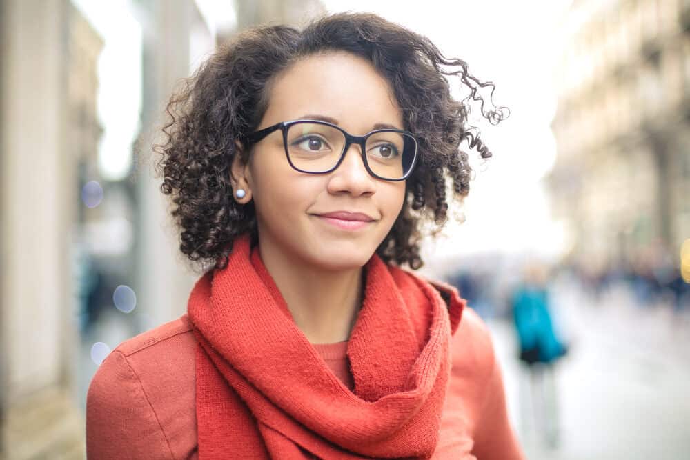 Female wearing naturally curly hair, black glasses, red lipstick, and silver earrings