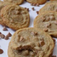 A white surface with caramel cookies and caramel baking chips on it, and a bite taken out of one of the cookies.