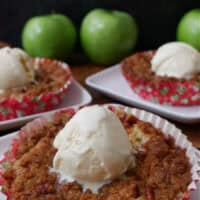 Three mini apple cobblers in red disposable cake liners with a scoop of vanilla ice cream on top.