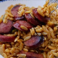 A white bowl with blue trim filled with a serving of smoked sausage and orzo pasta with the title of the recipe in text at the top.