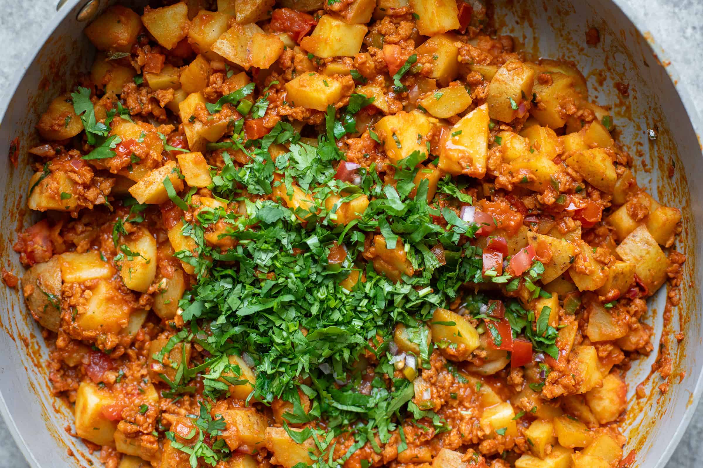 A Close-Up Of A Spicy Vegan Potato And Chorizo Dish In A Skillet, Garnished With Chopped Fresh Cilantro, Showcasing Vibrant Reds And Greens Against The Cooked Ingredients.