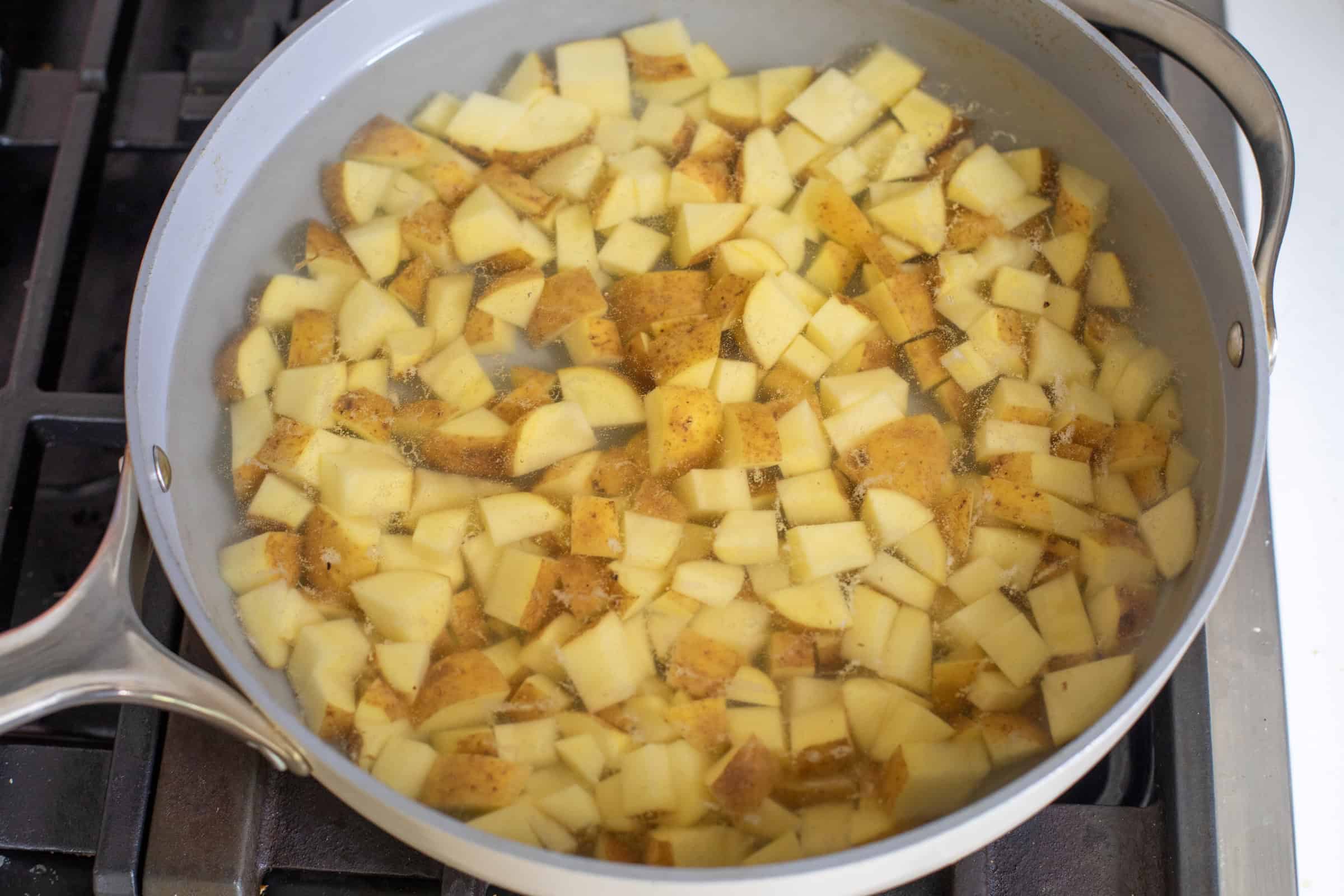 Diced Potatoes And Chorizo Cooking In A Skillet With Water And Spices On A Stove.