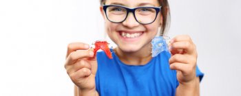 Grinning girl holding two dental retainers