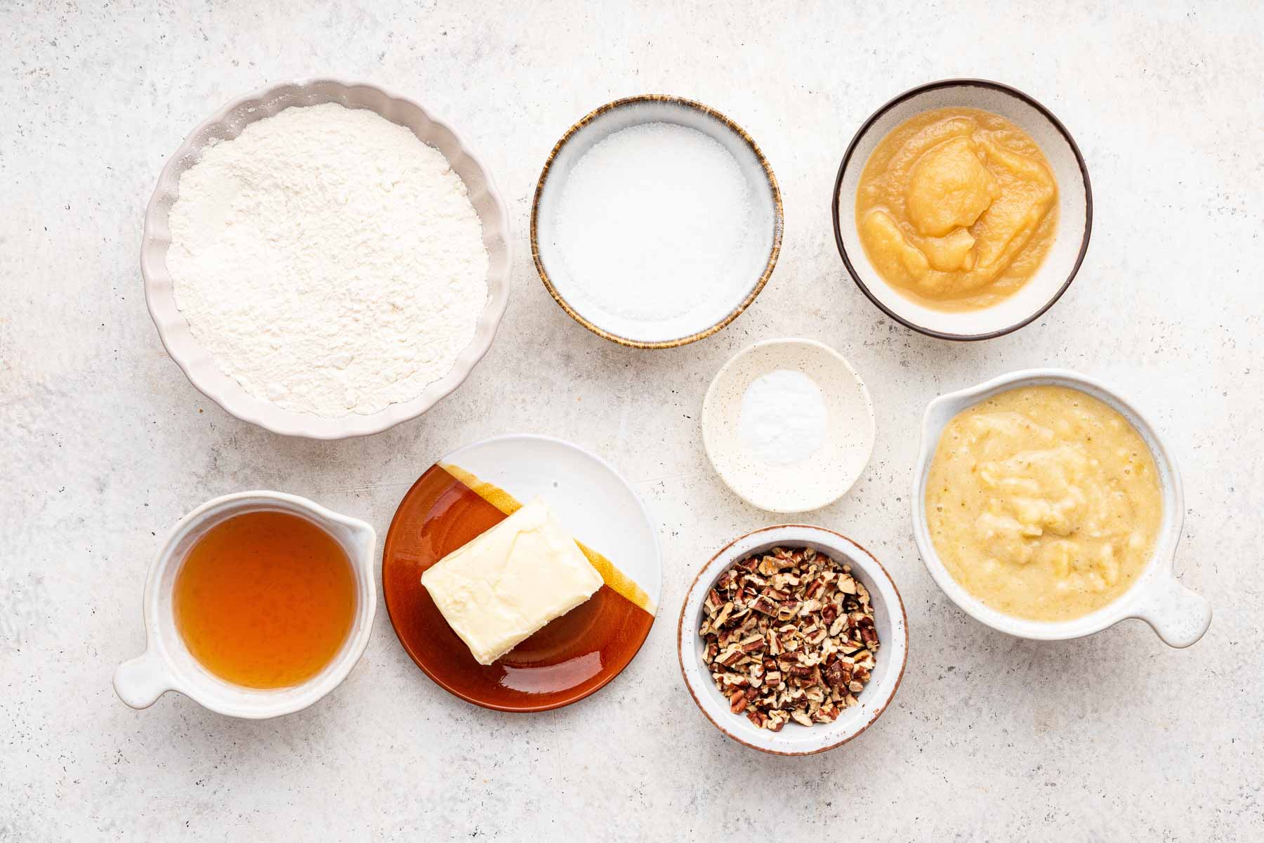 White bowls of baking ingredients on white counter.