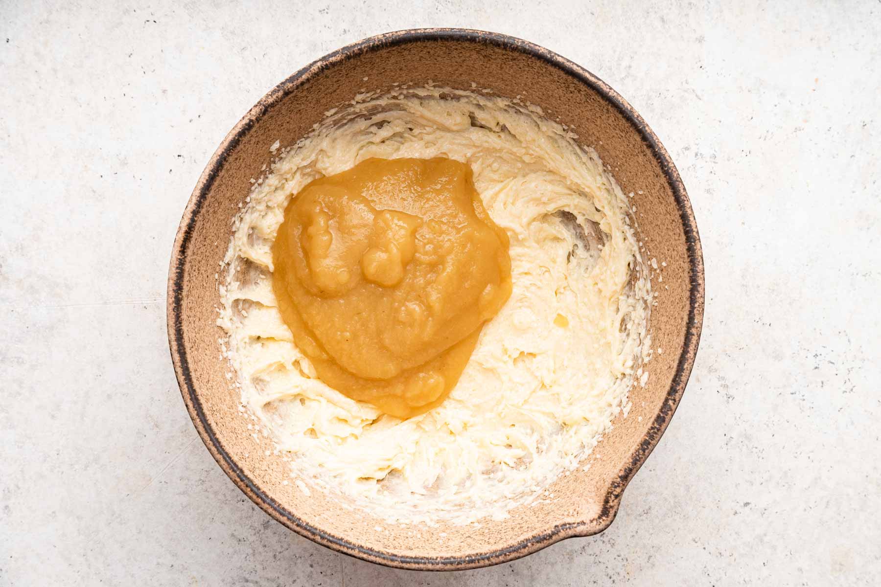 Honey and applesauce poured over creamed butter and sugar in brown bowl.