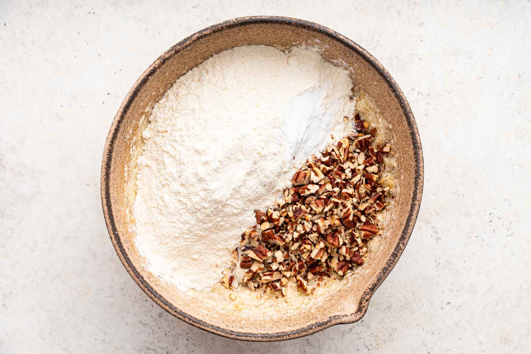 Flour and pecans sprinkled over yellow batter in mixing bowl.