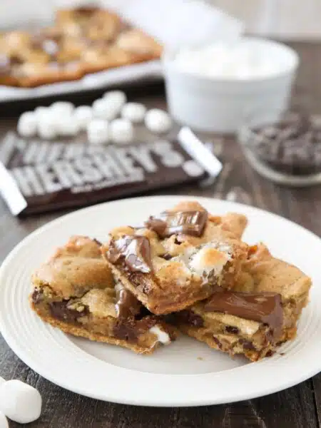 S'mores Cookie Bars are layered with graham crackers, cookie dough with marshmallows, and topped with chocolate bar pieces. It's an ooey gooey melty chocolate s'mores treat!