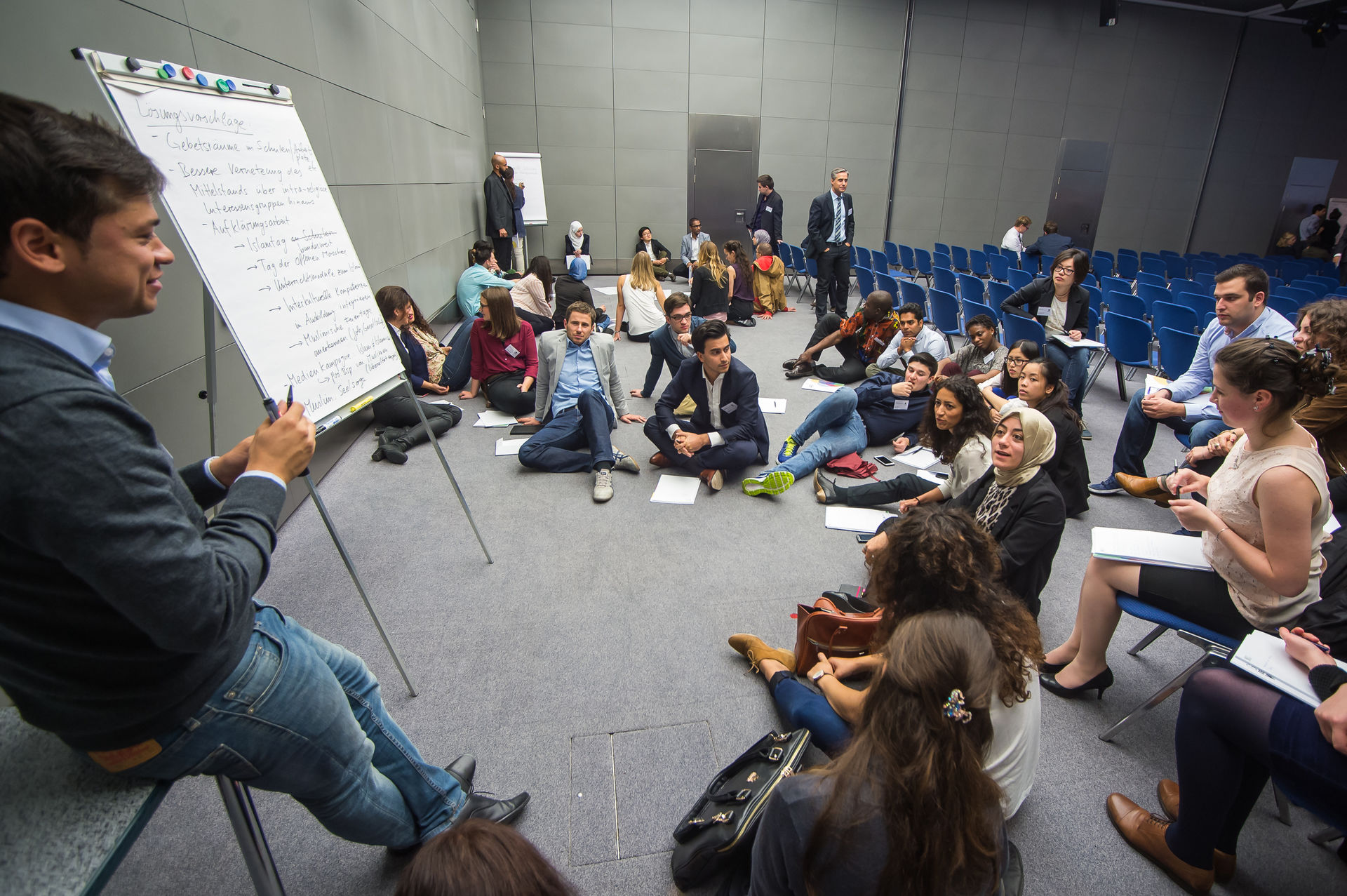 Workshop-Teilnehmer:innen in einem Sitzkreis um einen Flipchart 