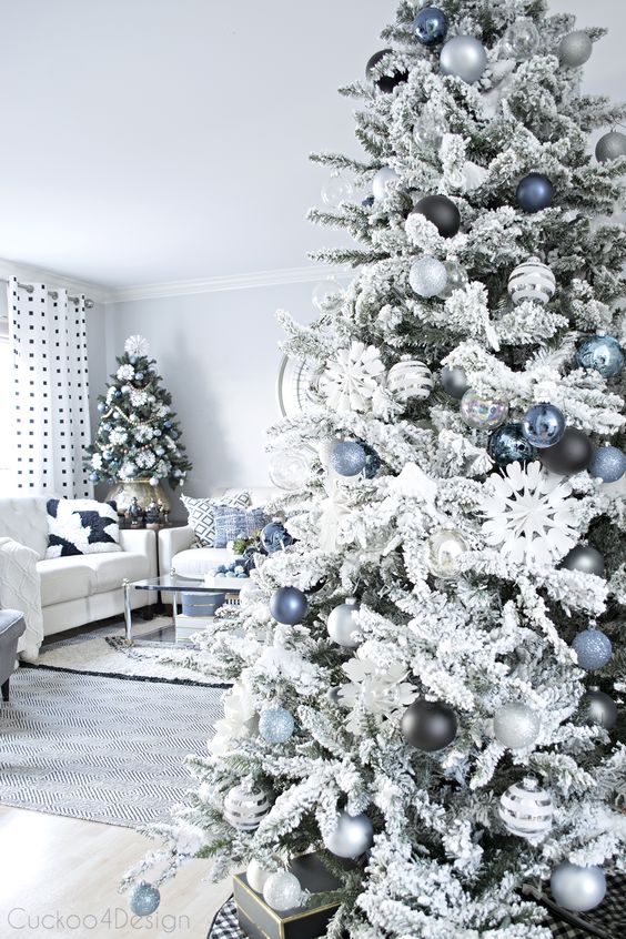 a flocked Christmas tree with blue, silver and black ornaments is a lovely and chic piece that looks frozen and elegant