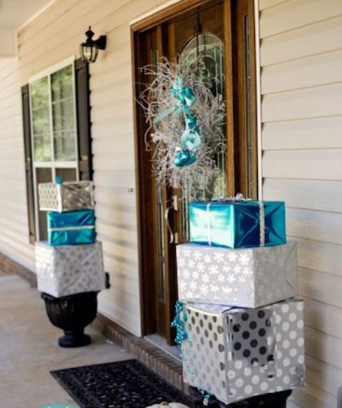 front porch Christmas decor with stacked silver and blue gift boxes and with a silver and blue wreath on the front door is amazing