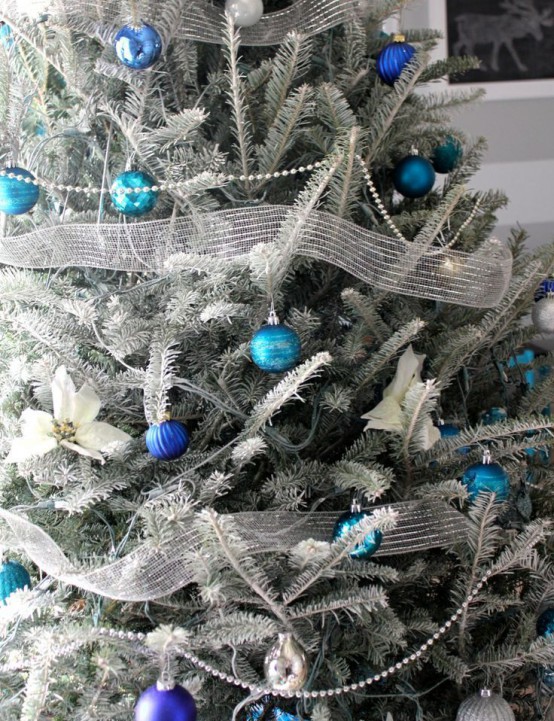 a frozen Christmas tree decorated with silver ribbons, blue, navy and black ornaments looks very spectacular and bold