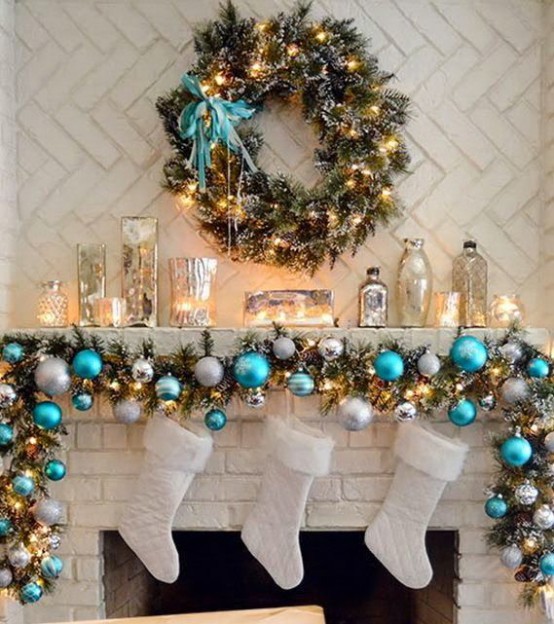 a fir garland with blue and silver ornaments plus lights, candles in mercury glass candleholders and a greenery wreath with lights and a turquoise bow