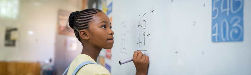 Black schoolgirl solving addition sum on white board with marker pen.