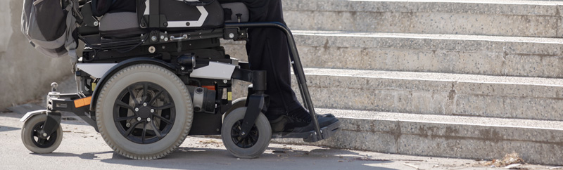 Person with disability on electric wheelchair stopping at the bottom of inaccessible staircase, unable to reach the top