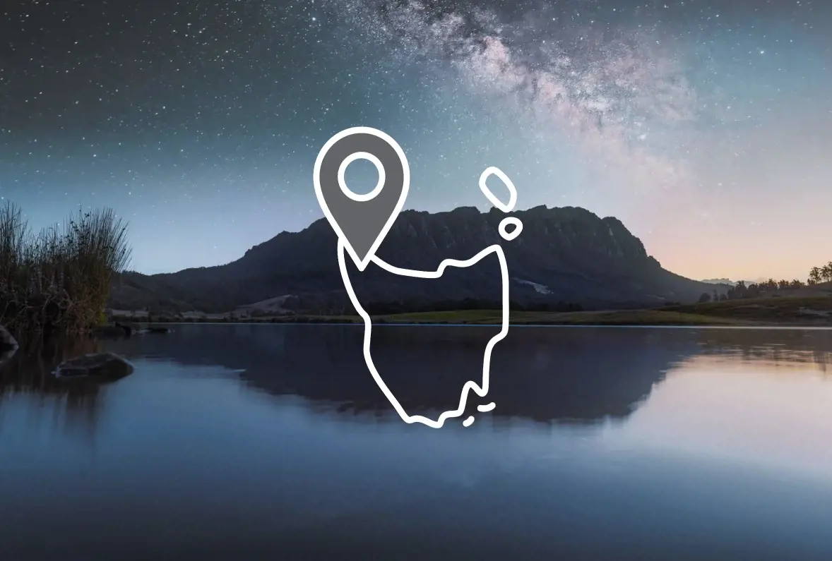 A mountain rises above a glassy lake, with the Milky Way visible in the sky. Overlaid is an icon of the outline of Tasmania with a map pin.