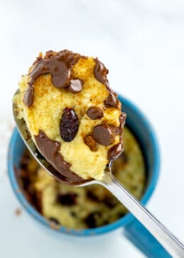 A spoon scooping out a piece of chocolate chip mug cookie from a blue cup.