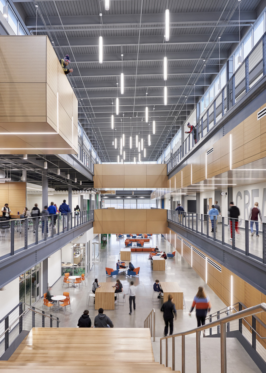 End of 2nd floor walkway looking down with views to 1st floor. Blue accents left, orange right. Pendant lights hang above