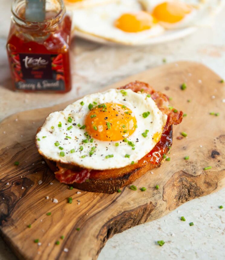 fried egg on toast on wooden board with chilli jam and fried eggs blurred in background