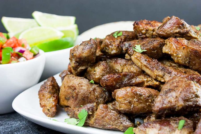 Crispy pork carnitas on a white platter garnished with chopped cilantro.