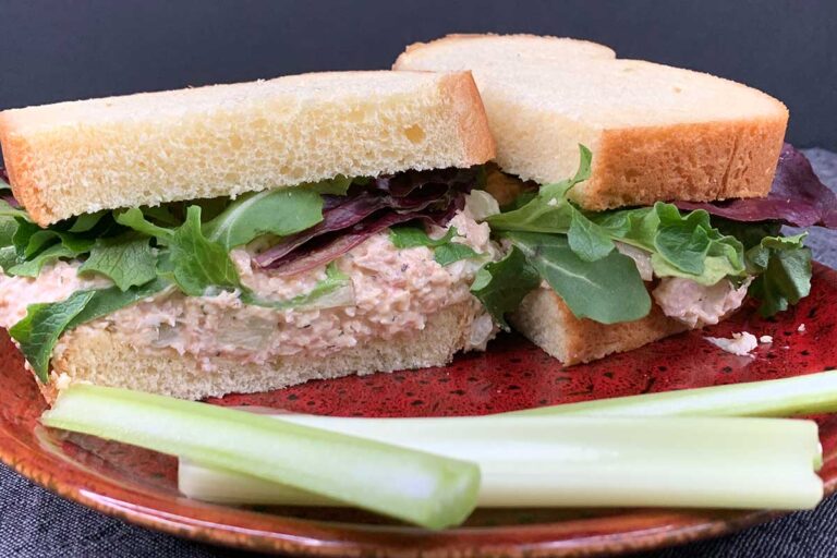 Smoked chicken salad sandwich on a red plate with celery sticks.