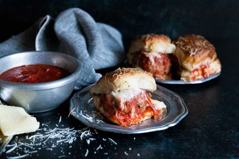 Meatball sliders on a silver plate garnished with shaved parmesan cheese.