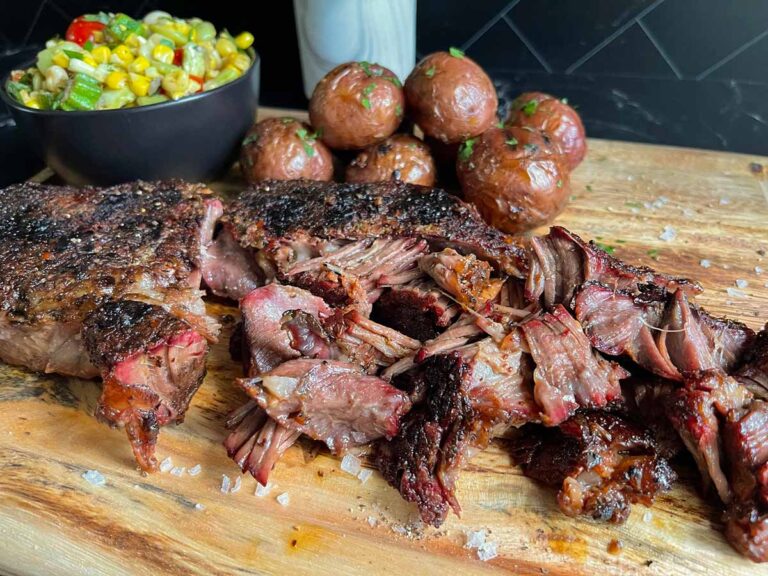 Smoked chuck roast with grilled potatoes and succotash on a wooden board.