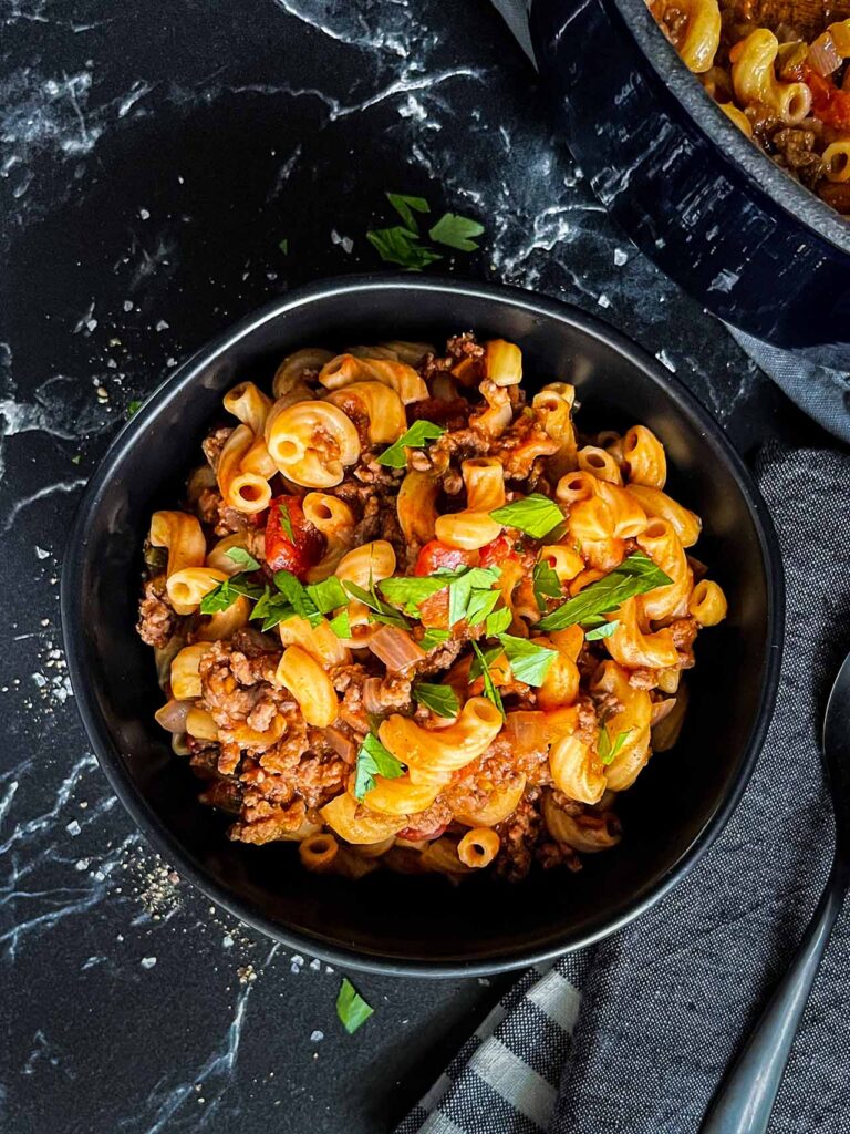 A bowl of goulash in a dark bowl.