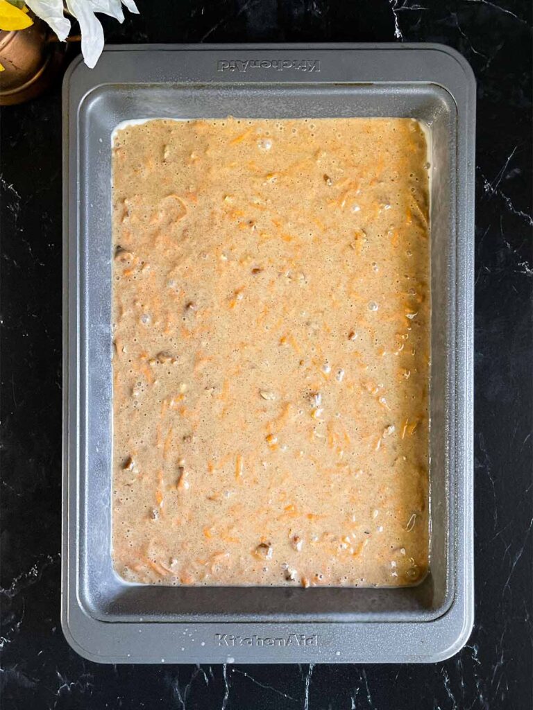 Sweet potato cake batter in a 9x13 baking pan on a dark surface.