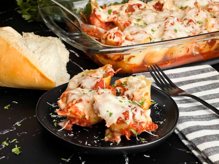 Italian stuffed shells on a black plate with some bread and a casserole dish in the background.