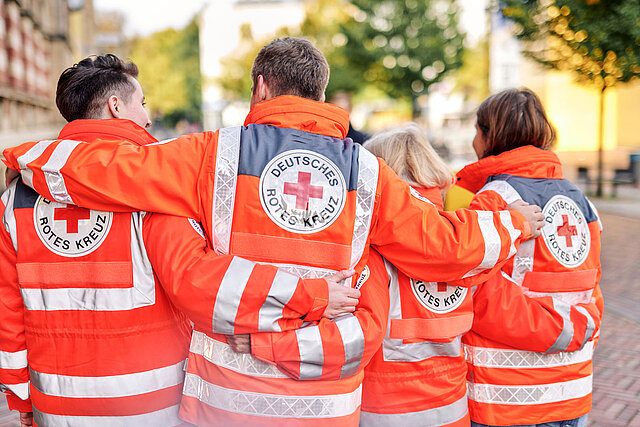 Vier DRKler in Einsatzjacken legen Arme über Schultern