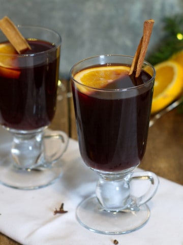 Two glass mugs filled with mulled red wine and garnished with cinnamon sticks and orange.