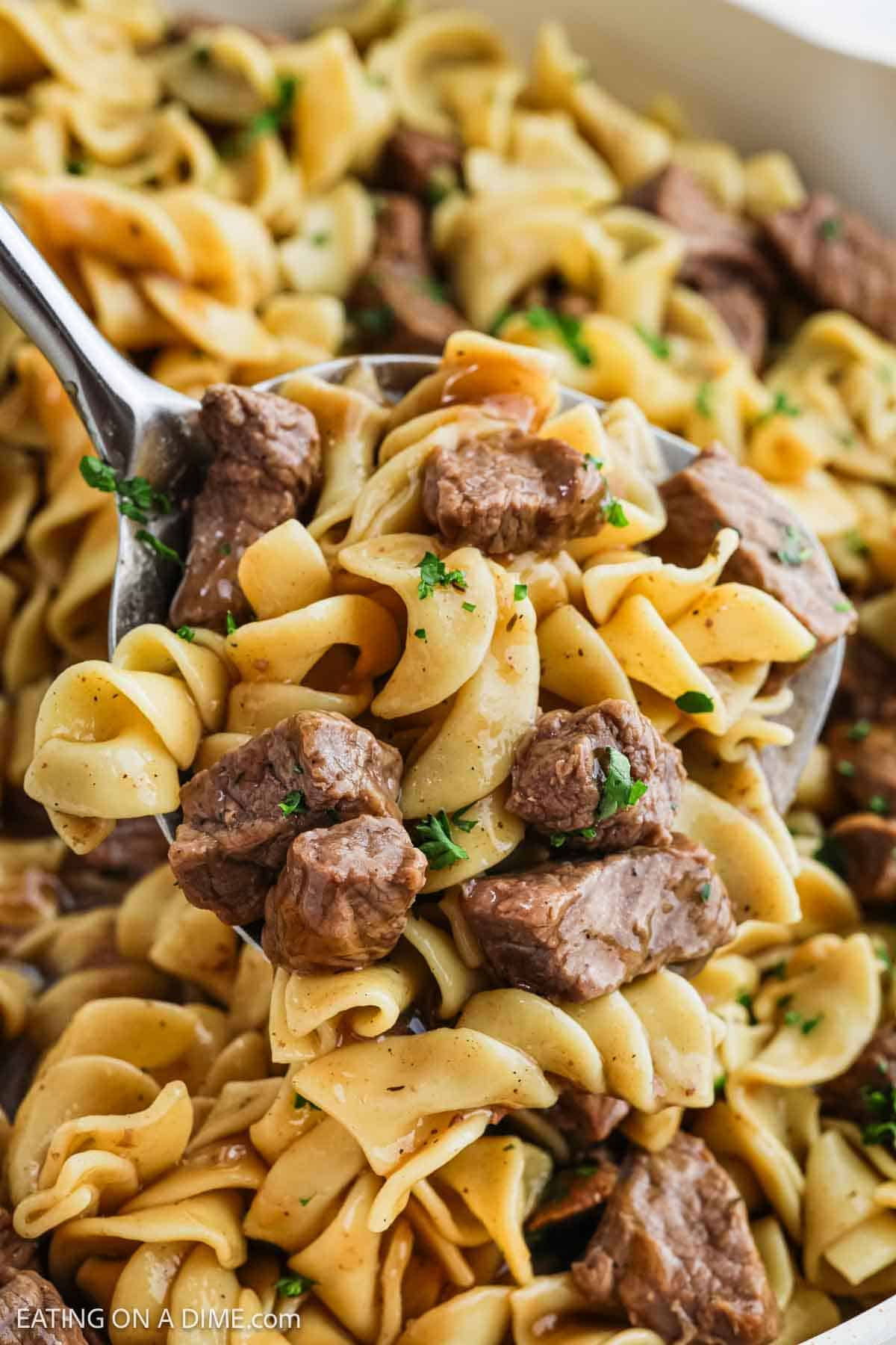 Beef Tips and Noodles on a silver spoon with beef tips and noodles in a skillet 