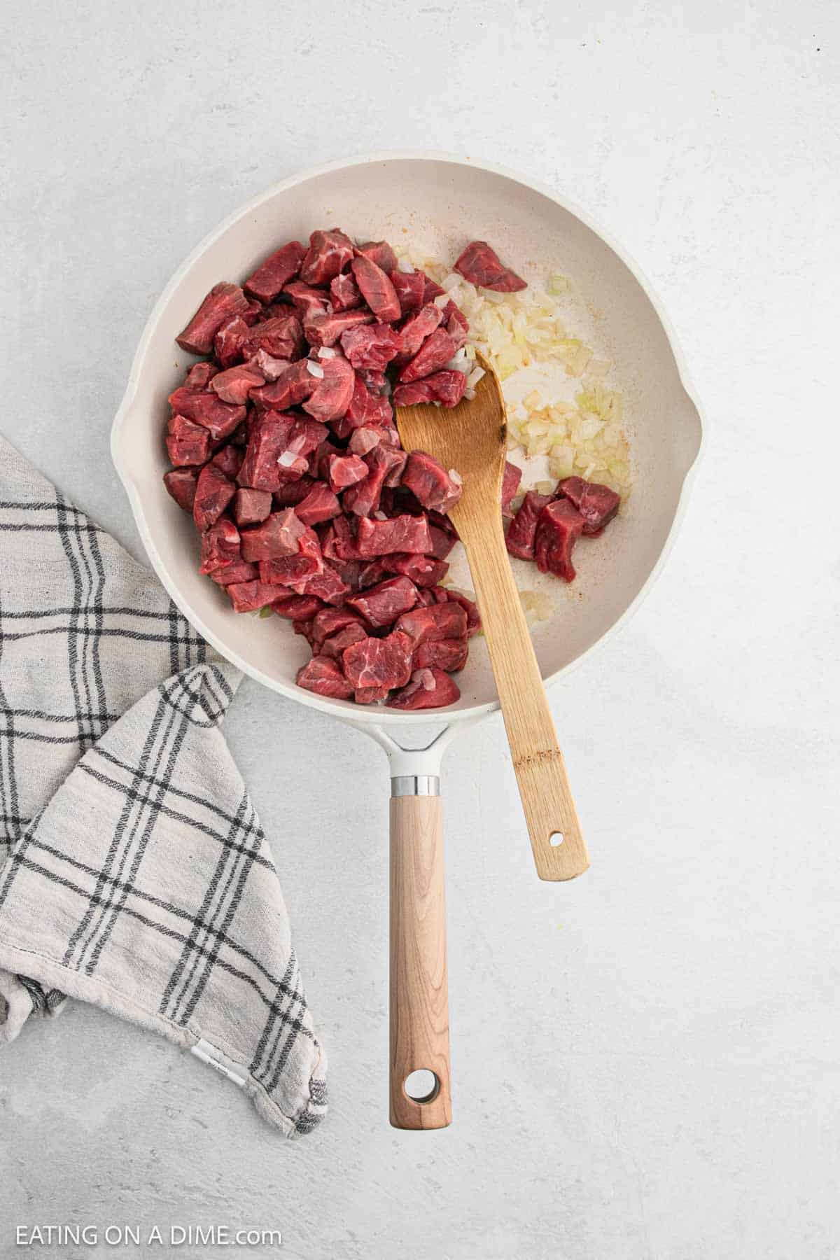 Beef Tips in a skillet with cooked chopped onions with a wooden spoon