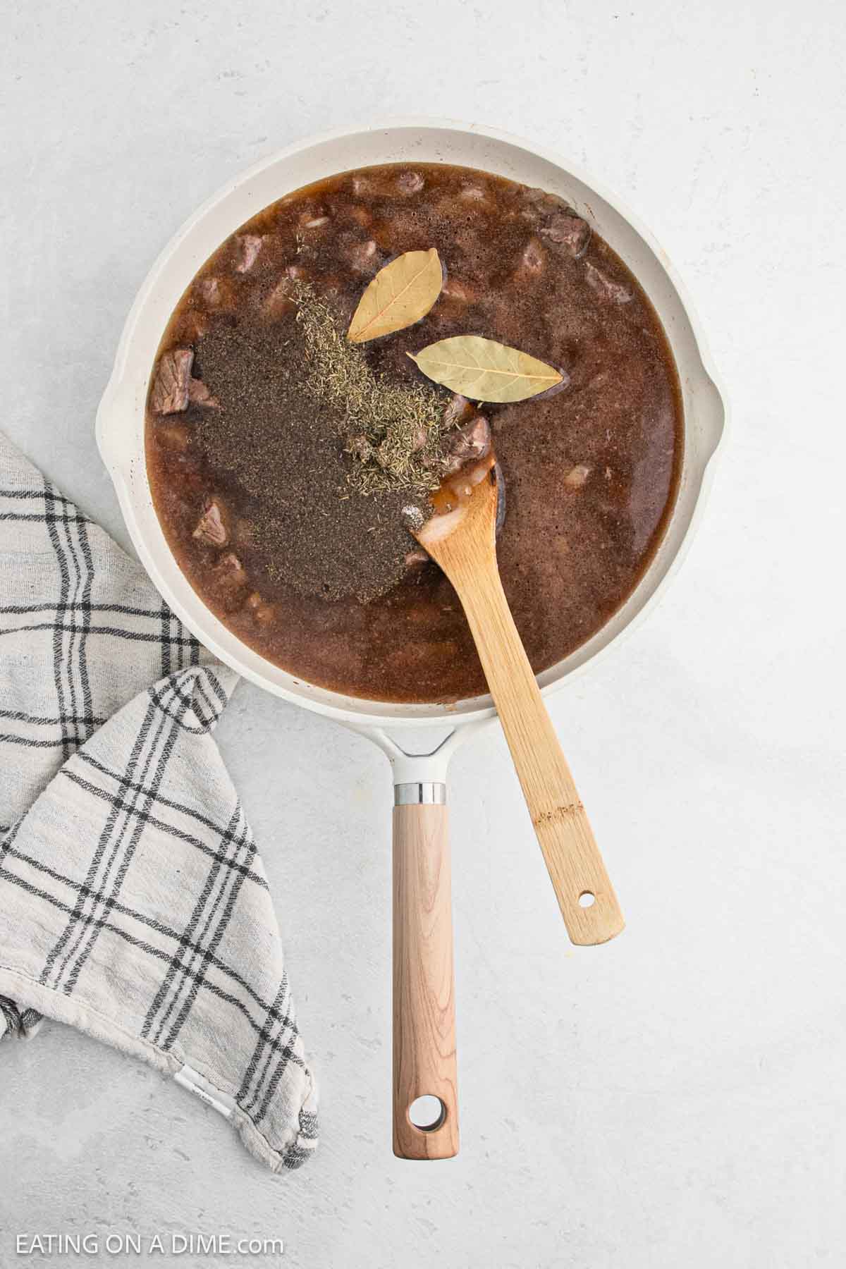 Bay leaf and seasoning topped on the broth and beef tips in a skillet