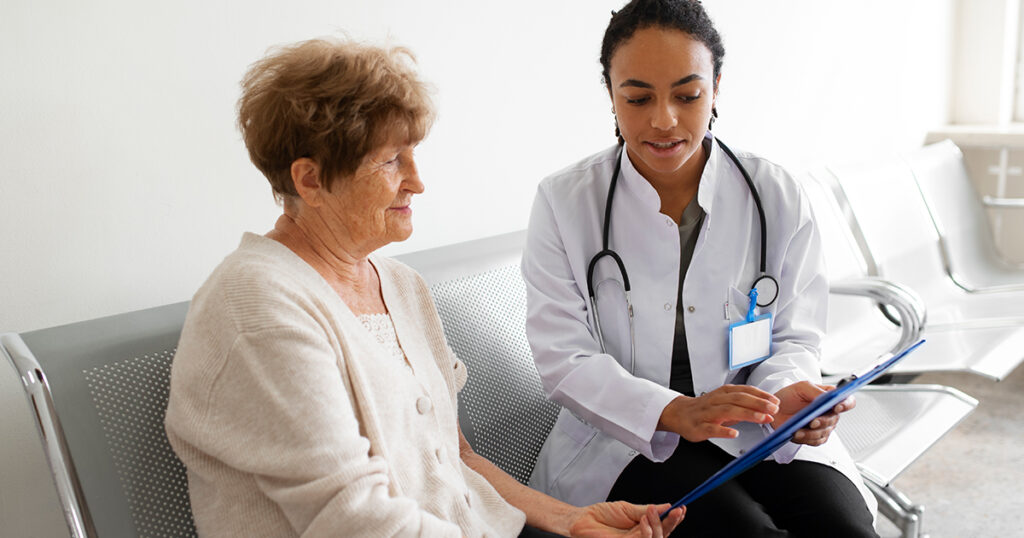 A female doctor sits with a female patient on a metal bench and discusses health care options and home health indicators