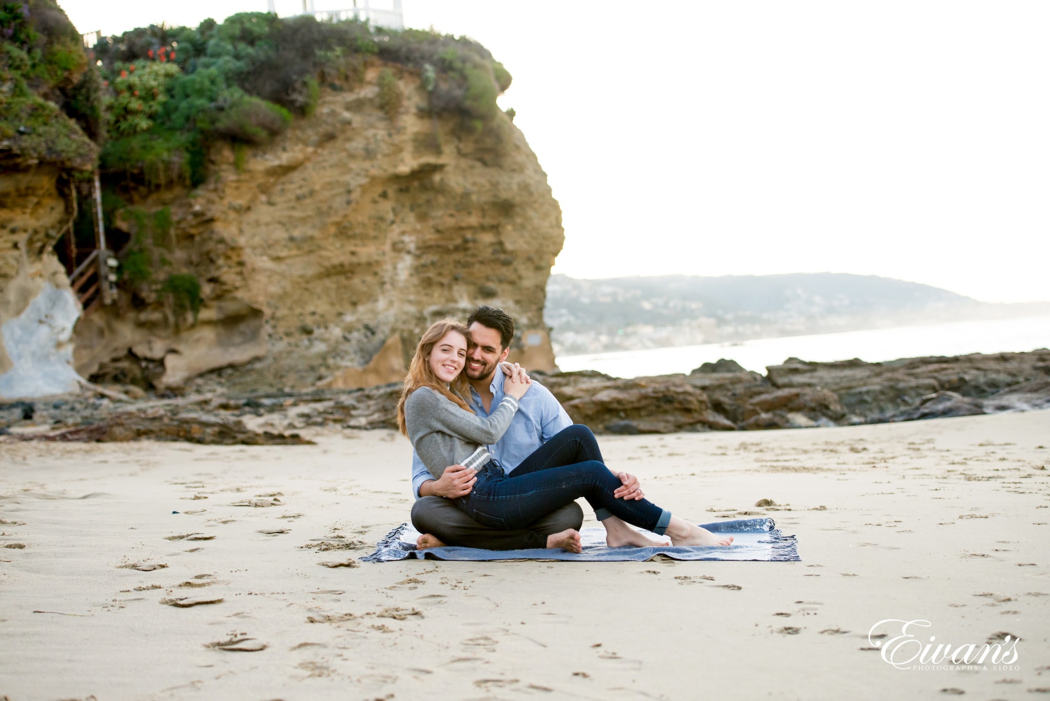 woman in gray long sleeve shirt and black pants sitting on white sand during daytime