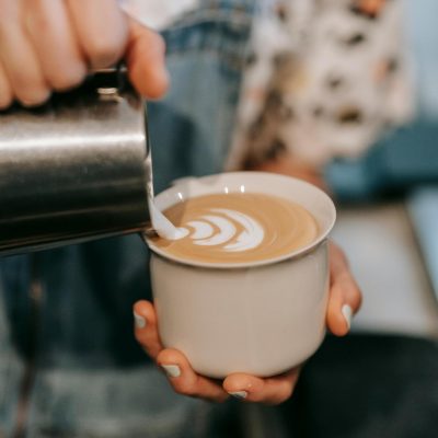 Woman holding a cup of coffee while poring creamer in.