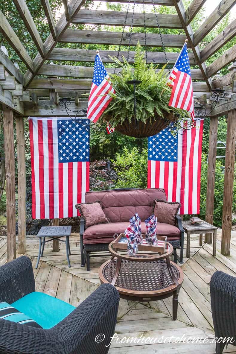 Large American flags hanging from the side of a gazebo with a hanging fern and small flags inside