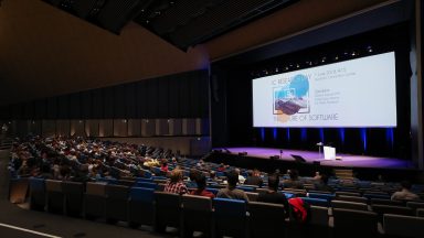 Intérieur du SwissTech Convention Center durant la ournée de la recherche IC. la salle est plongée dans le noir. Une présentation est en cours sur la scène.