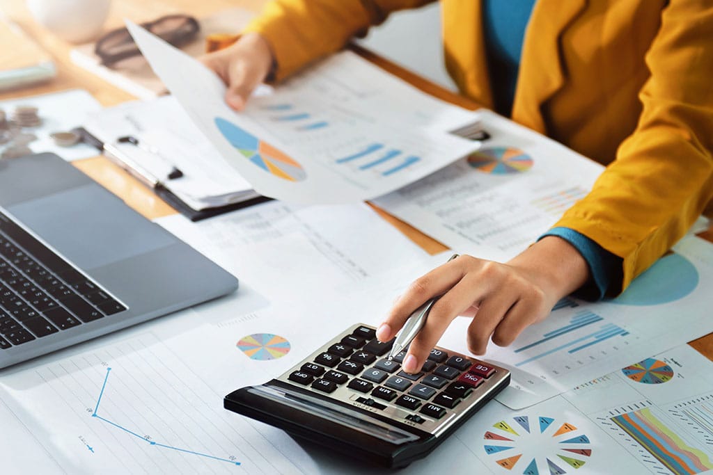 Woman does calculations while looking at financial reports and graphs.