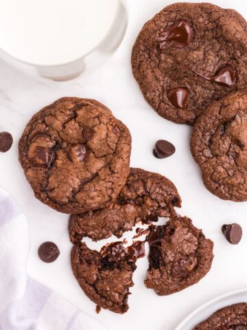 Overhead view of several cookies and a glass of milk. One cookie is broken up to show the gooey interior.