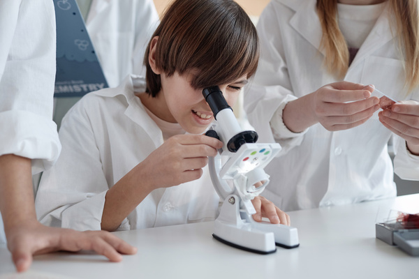 A Group of Kids in Lab Coats Looking through a Microscope