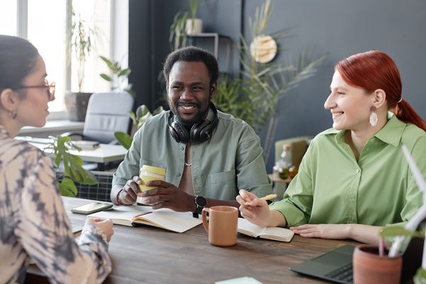 Three People Having a Conversation at a Desk with a Laptop and Coffee