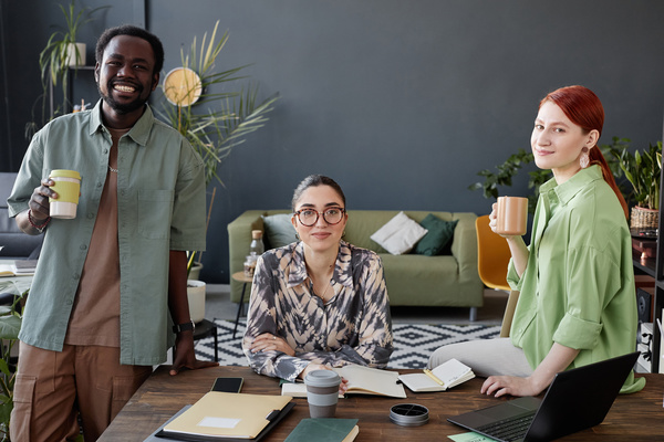 Three People Sitting at a Desk with a Laptop and Coffee Cups