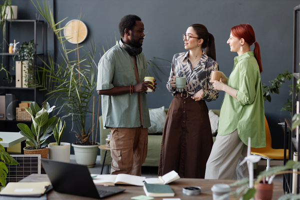 Three People Standing in an Office with Potted Plants and Laptops