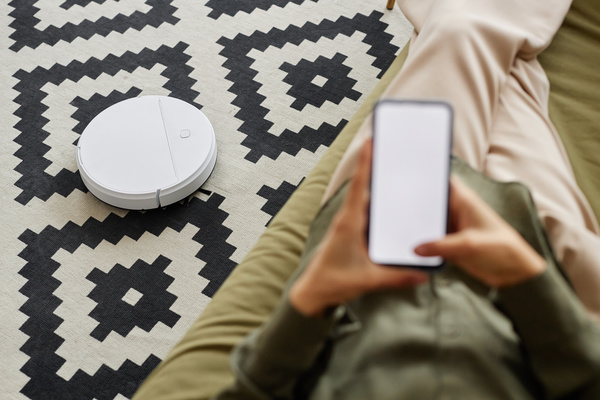 A Person Sitting on a Couch Next to a Robot Vacuum