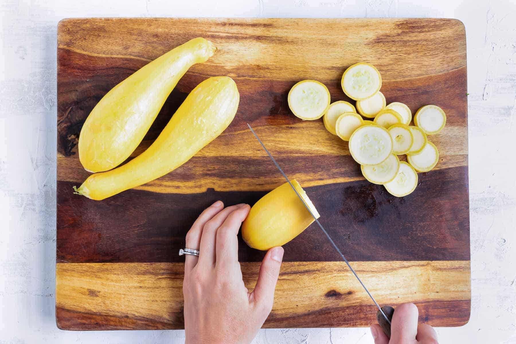 A hand carefully slices a yellow squash into thin slices.