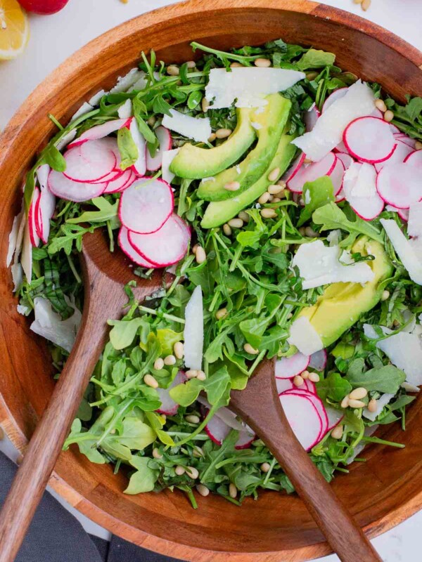 Salad tongs toss a lemon arugula salad together.