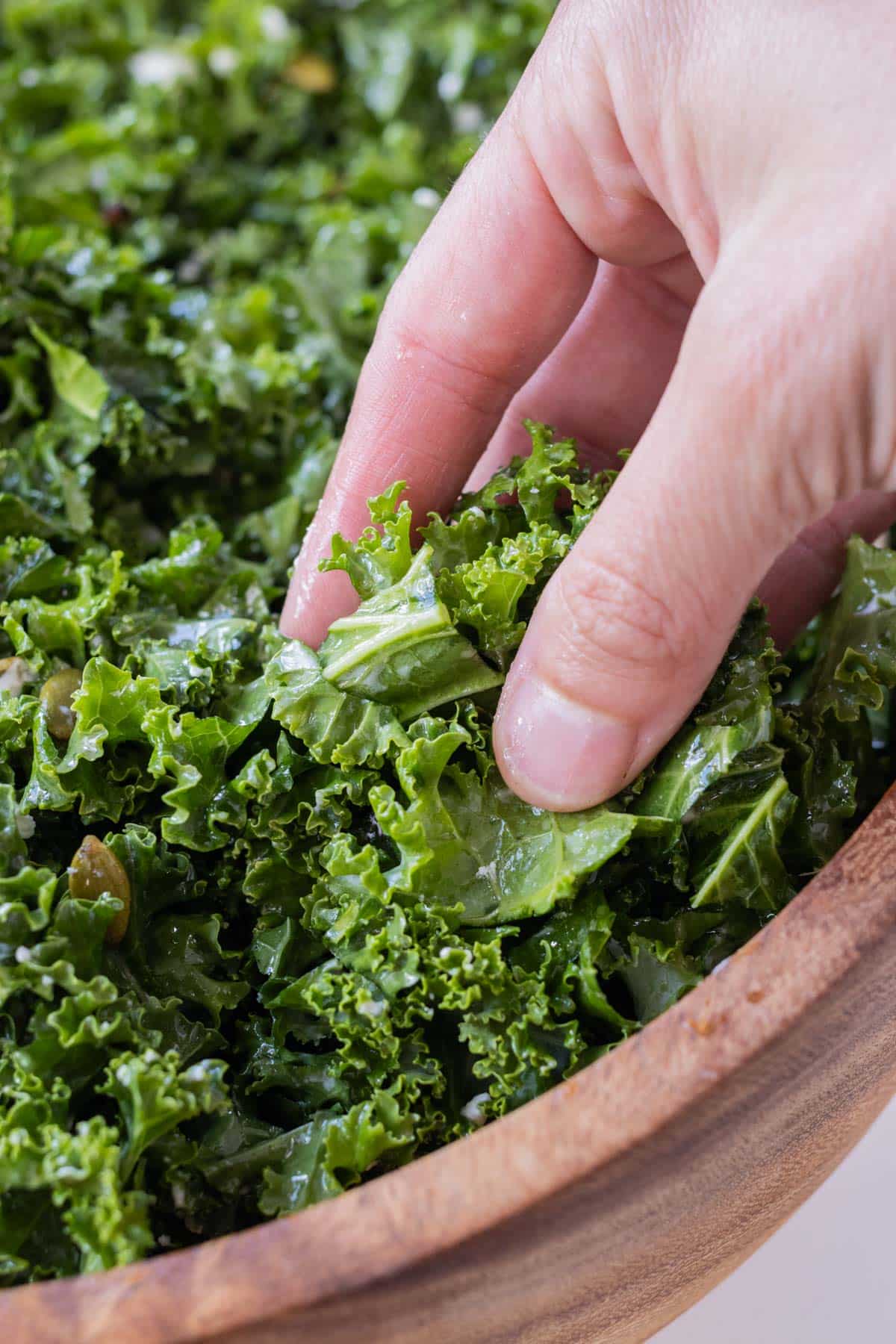 Maple vinaigrette is being rubbed into kale leaves to make them tender for a salad.