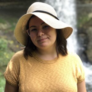 Marissa in yellow dress and sunhat smiles in front of waterfall